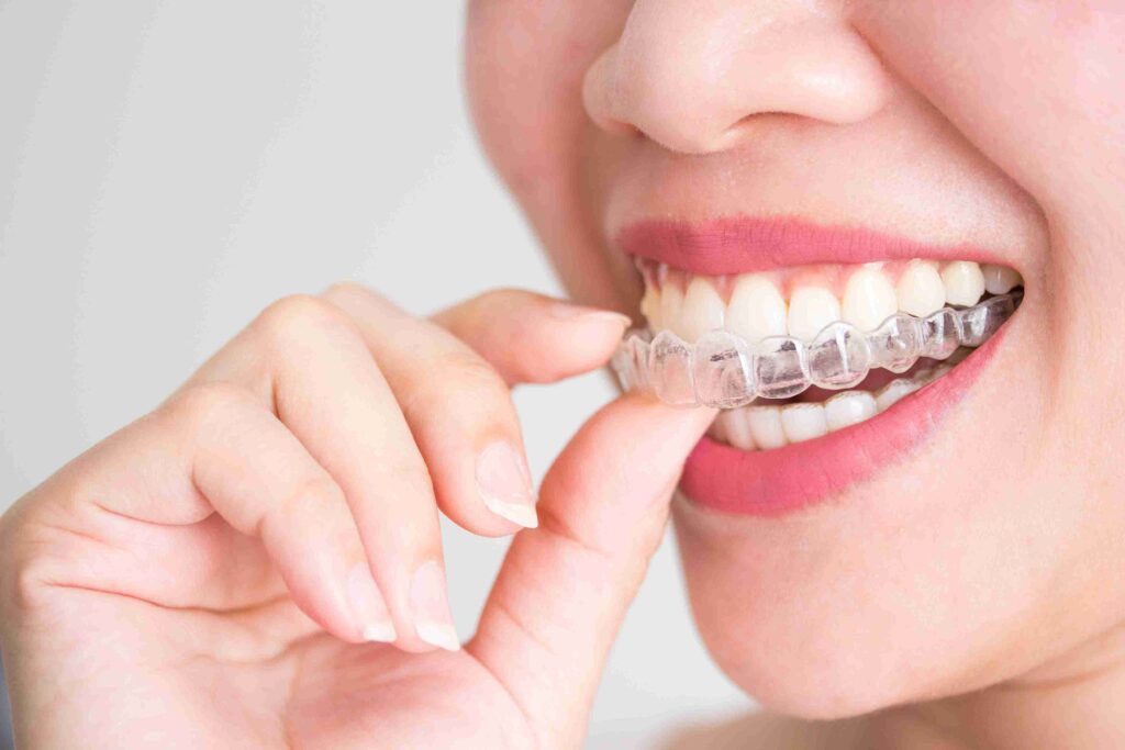 A patient holding a clear Invisalign aligner tray in front of a confident smile at Aghbashian Dental in Glendale, CA 91202, demonstrating discreet orthodontic treatment.